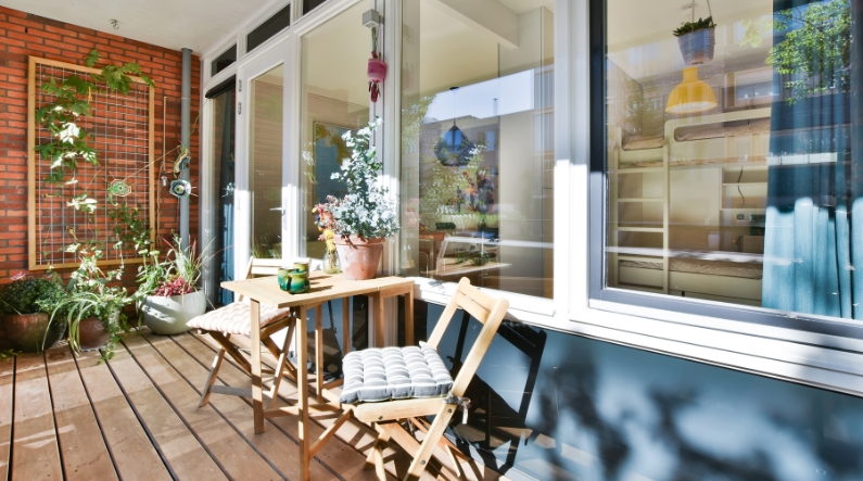 Veranda con pavimento in legno, piante, tavolino e sedute in legno.